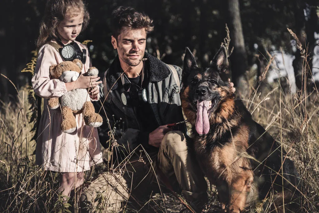 Handsome man touching german shepherd dog near kid with teddy bear, post apocalyptic concept